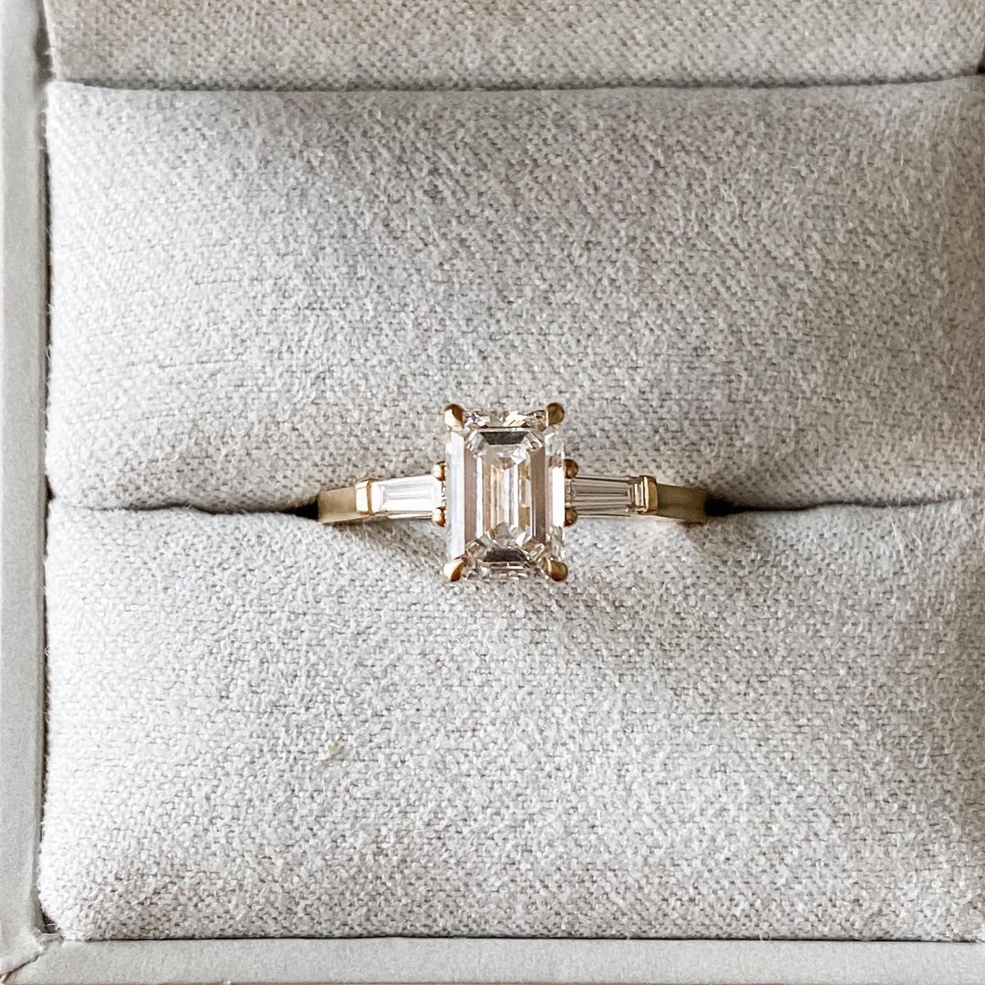 2.5ct Emerald Center Stone With Two Side Baguette Stone Lab Grown Diamond Ring youtube google instagram Elegant close-up of a hand showcasing an engagement ring with a gold band, ideal for proposals, weddings, or luxury jewelry collections, paired with a soft, natural manicure.